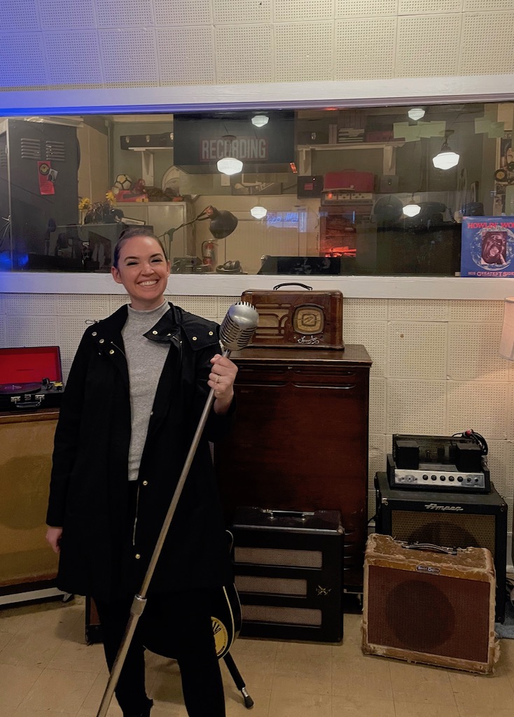 Woman smiling and holding 1950s era recording microphone in old record studio. Sun Studio, Memphis, Tennessee.