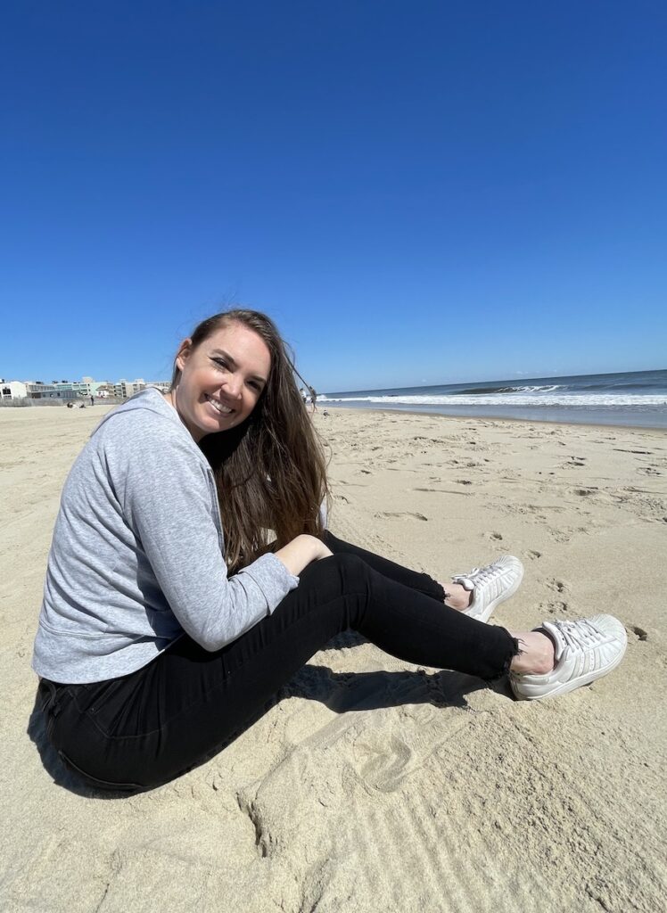 Woman smiling on white sand beach with ocean and blue skies in background. Rehoboth Beach, Rehoboth Beach, Delaware.