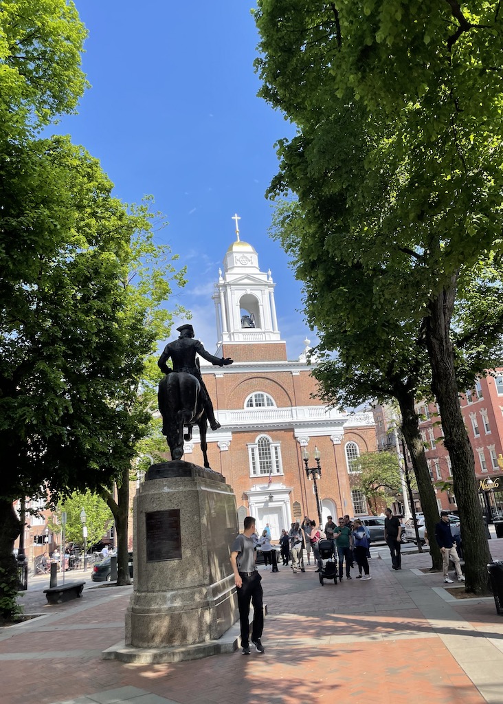 Large statue of man on horse on wide walkway with brick church in background on sunny summer day. Paul Revere Mall, Old North Church, North End, Boston, Massachusetts, New England.
