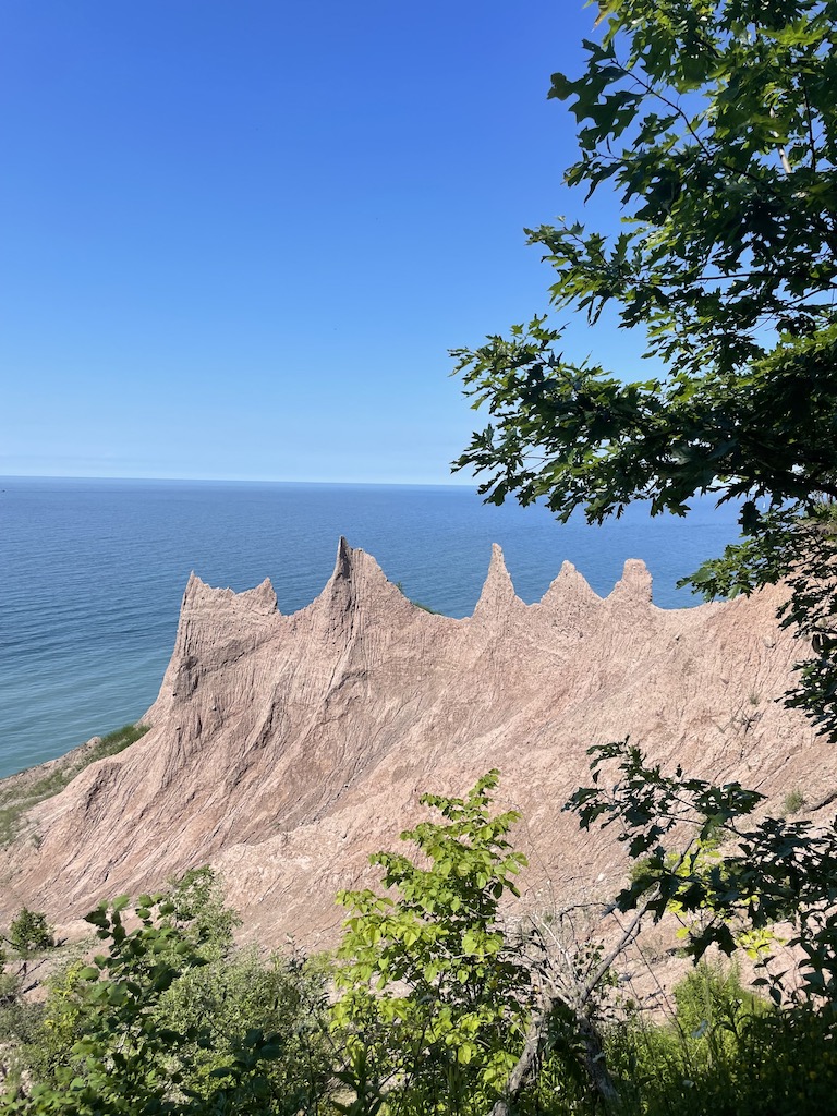 Tan colored rock formation overlooking huge blue lake on bright sunny day. Chimney Bluffs State Park, Lake Ontario, Upstate, New York.